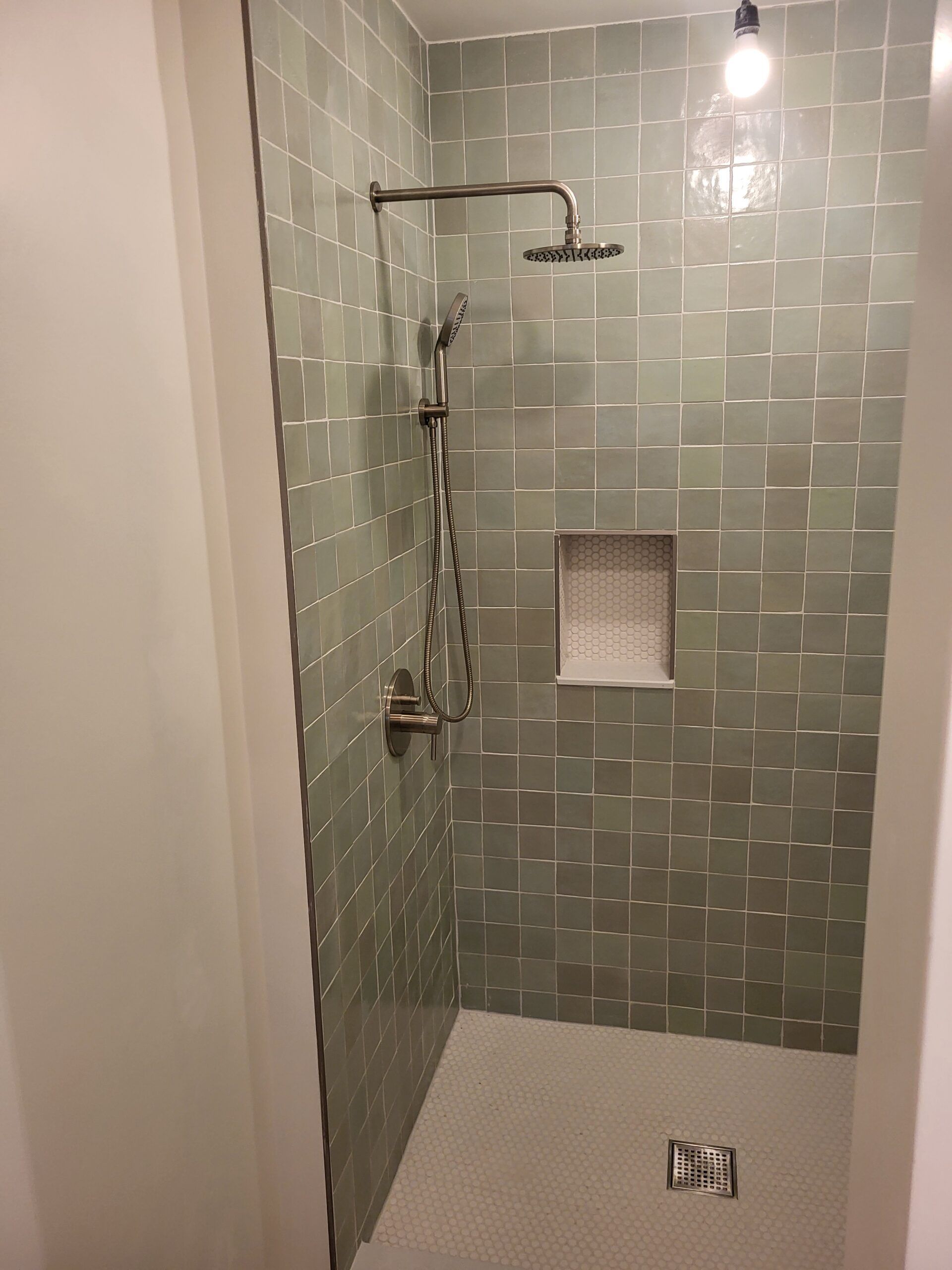 Shower with green square tiles and silver fixtures, white floor, and a built-in niche.