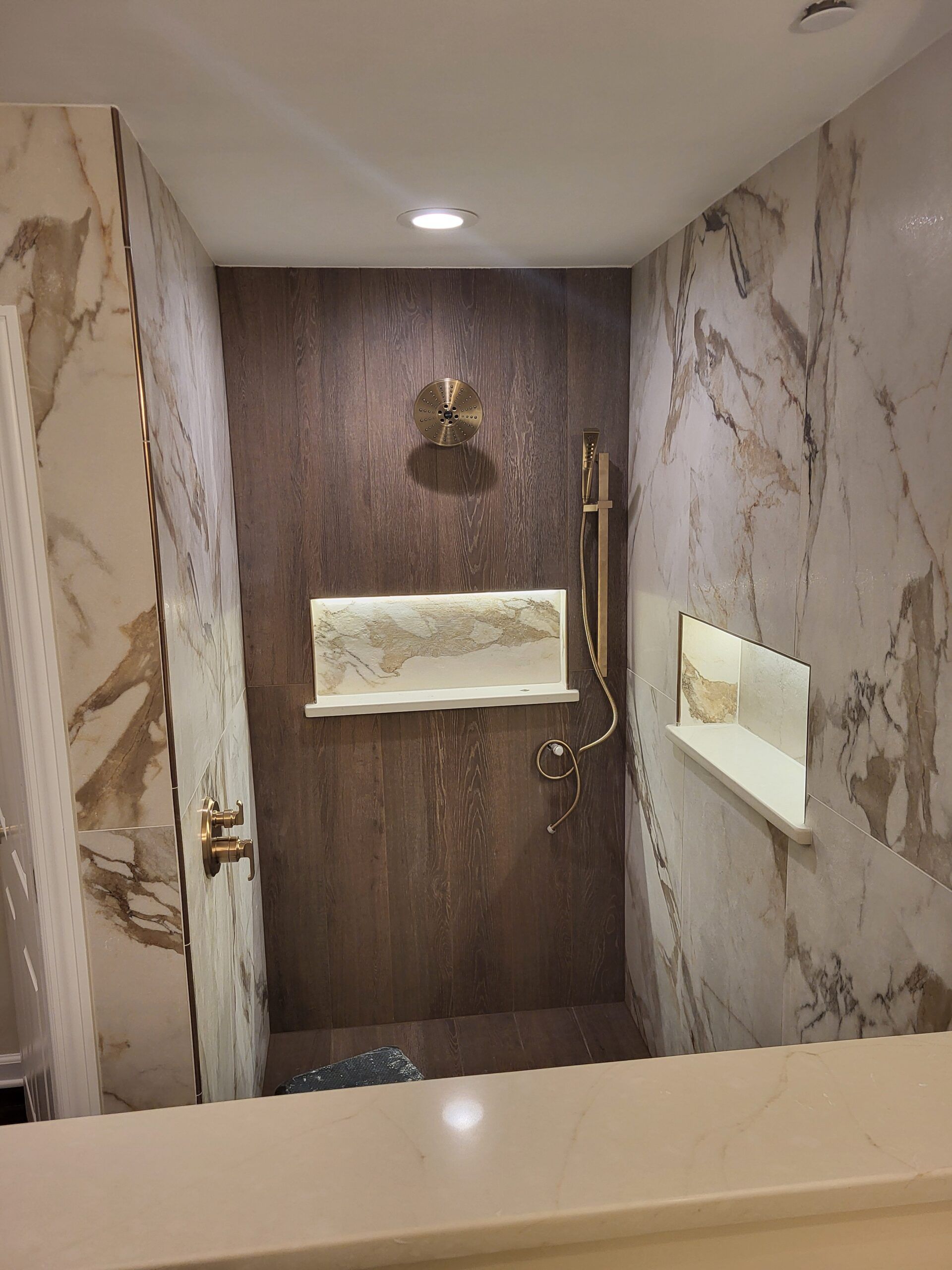 Shower with marble walls and a dark brown accent wall, featuring gold fixtures and built-in shelves.