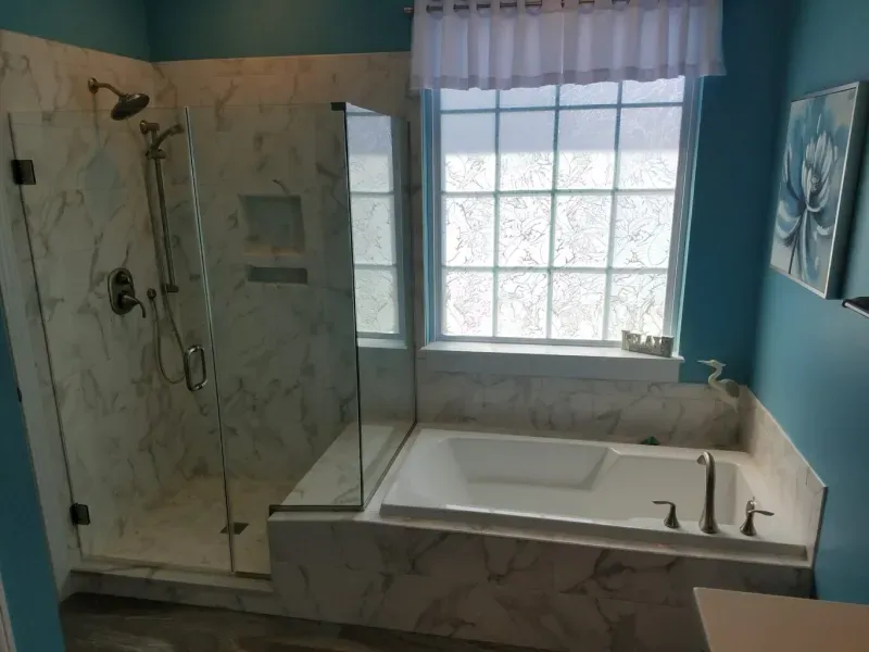 A modern bathroom with a marble-tiled shower, a built-in tub, and a window with light blue walls.