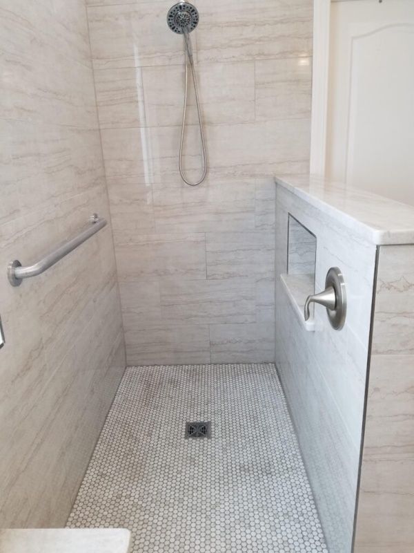 Walk-in shower with light-colored marble-style tiles, a built-in bench, and a grab bar for accessibility.