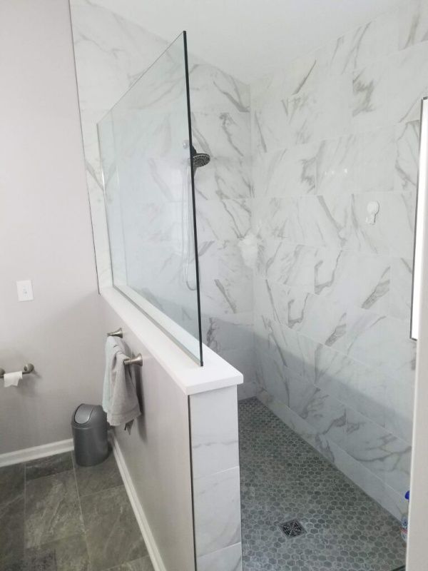 A modern bathroom with a glass shower enclosure. The shower has marble-look tiled walls and floor. A towel rack and toilet are visible.