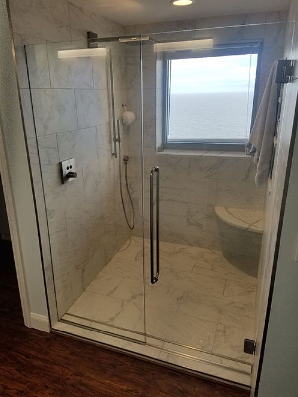 A modern shower with marble-like tile, glass doors, and a window. A towel hangs nearby.