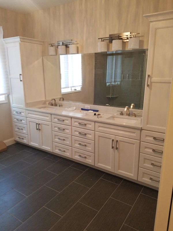 Bathroom with white cabinets, long marble countertop, dark gray floor, and large mirror with lighting fixtures.