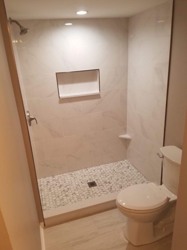 Bathroom with a tiled shower, a pebble floor, and a toilet. White and gray tiles are used throughout.
