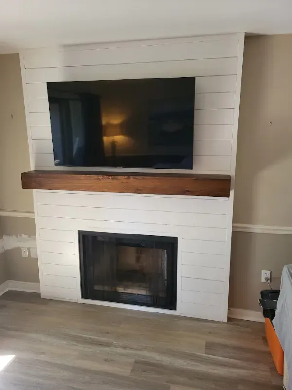 A white shiplap fireplace with a dark-framed firebox, a stained wooden mantel, and a mounted black TV.