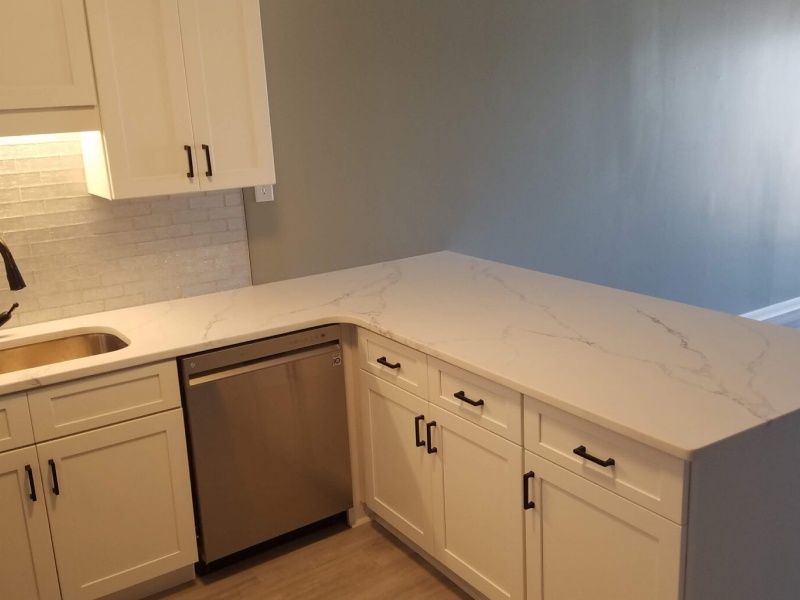A modern kitchen with white cabinets, a stainless steel dishwasher, and a white countertop with gray veining.