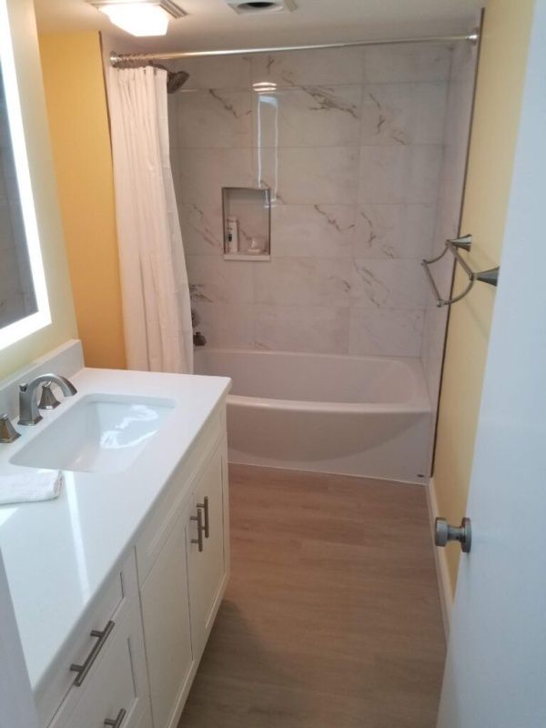 A bright bathroom with a white vanity, beige floor, and a white-tiled shower/tub area. The walls are painted yellow.