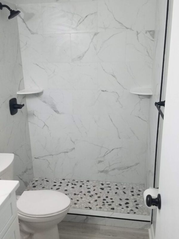 Bathroom with marble-look shower tiles, pebble floor, and a white toilet. Black shower fixtures.