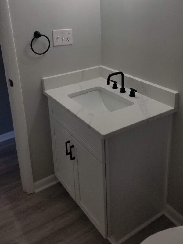 White bathroom vanity with black hardware and faucet. Gray walls, light countertop, and a towel ring.