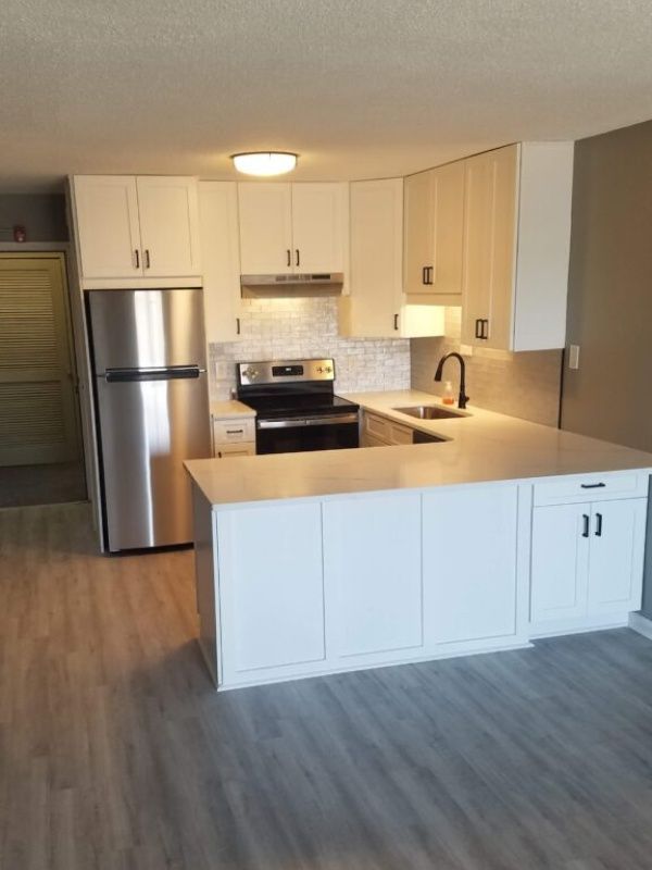 Modern white kitchen with stainless steel appliances, light countertops, and gray flooring.