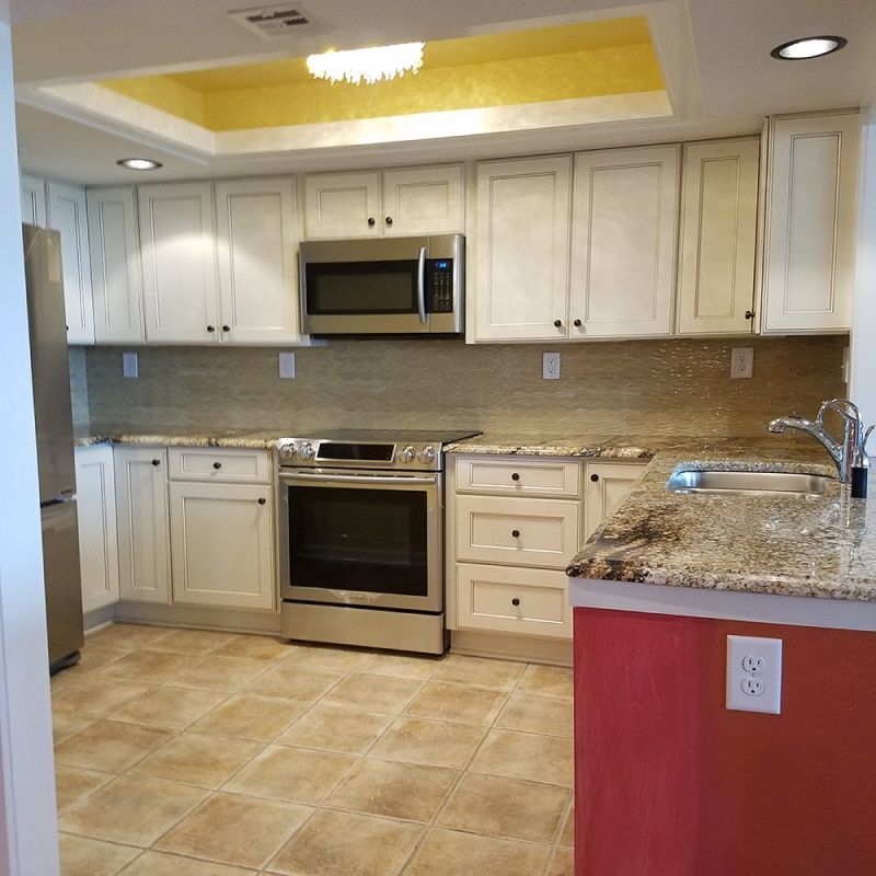 A kitchen with white cabinets, stainless steel appliances, and tan countertops. The walls are a light tan with a red accent.