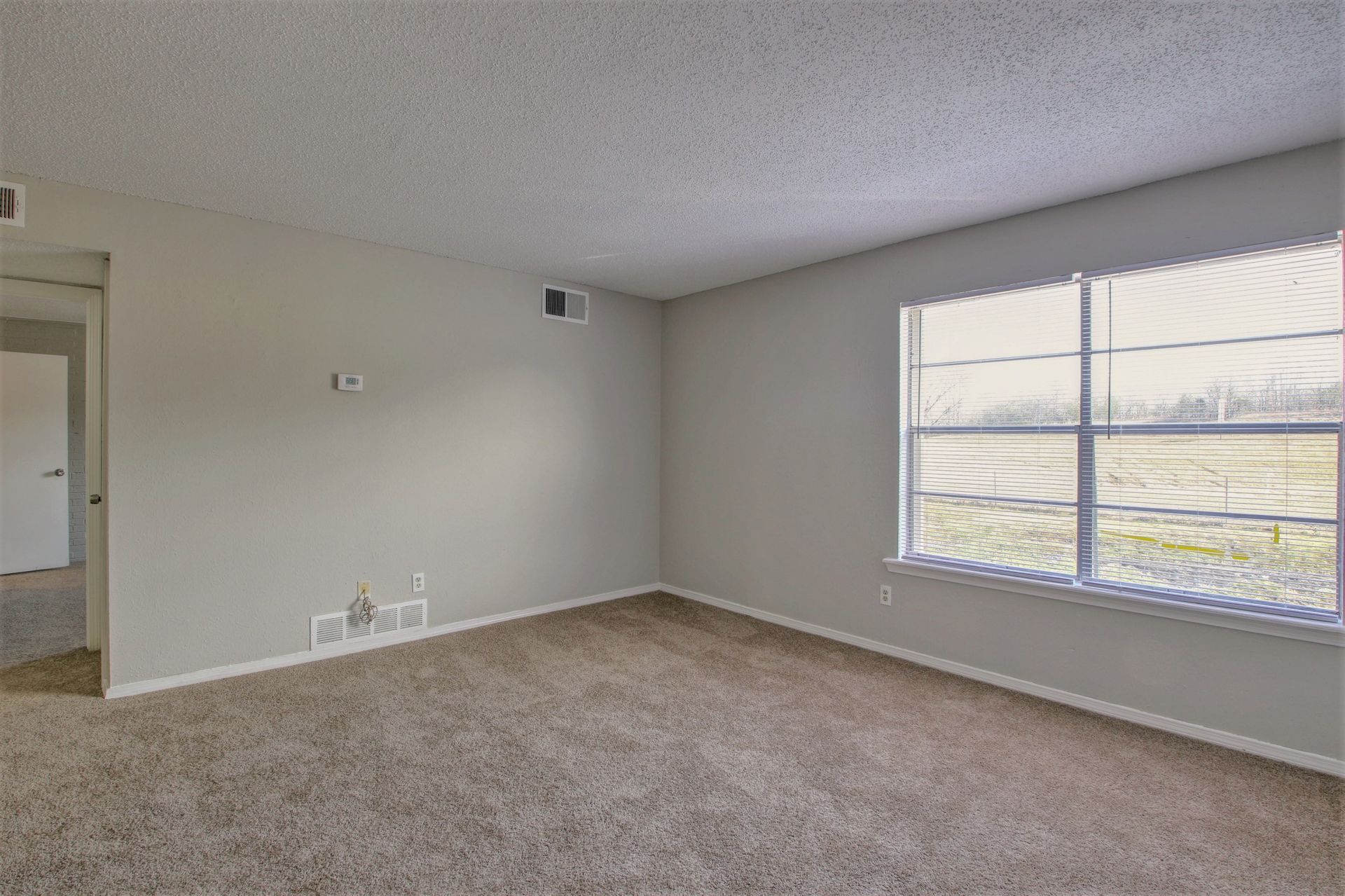 An empty living room with a large window and a carpeted floor.