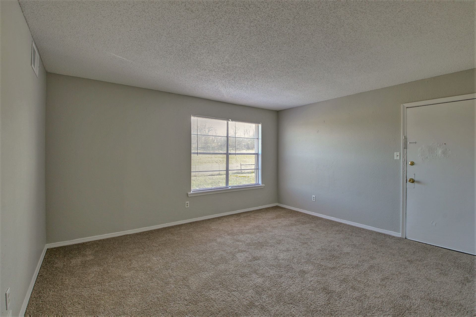 An empty room with a window and a carpeted floor.
