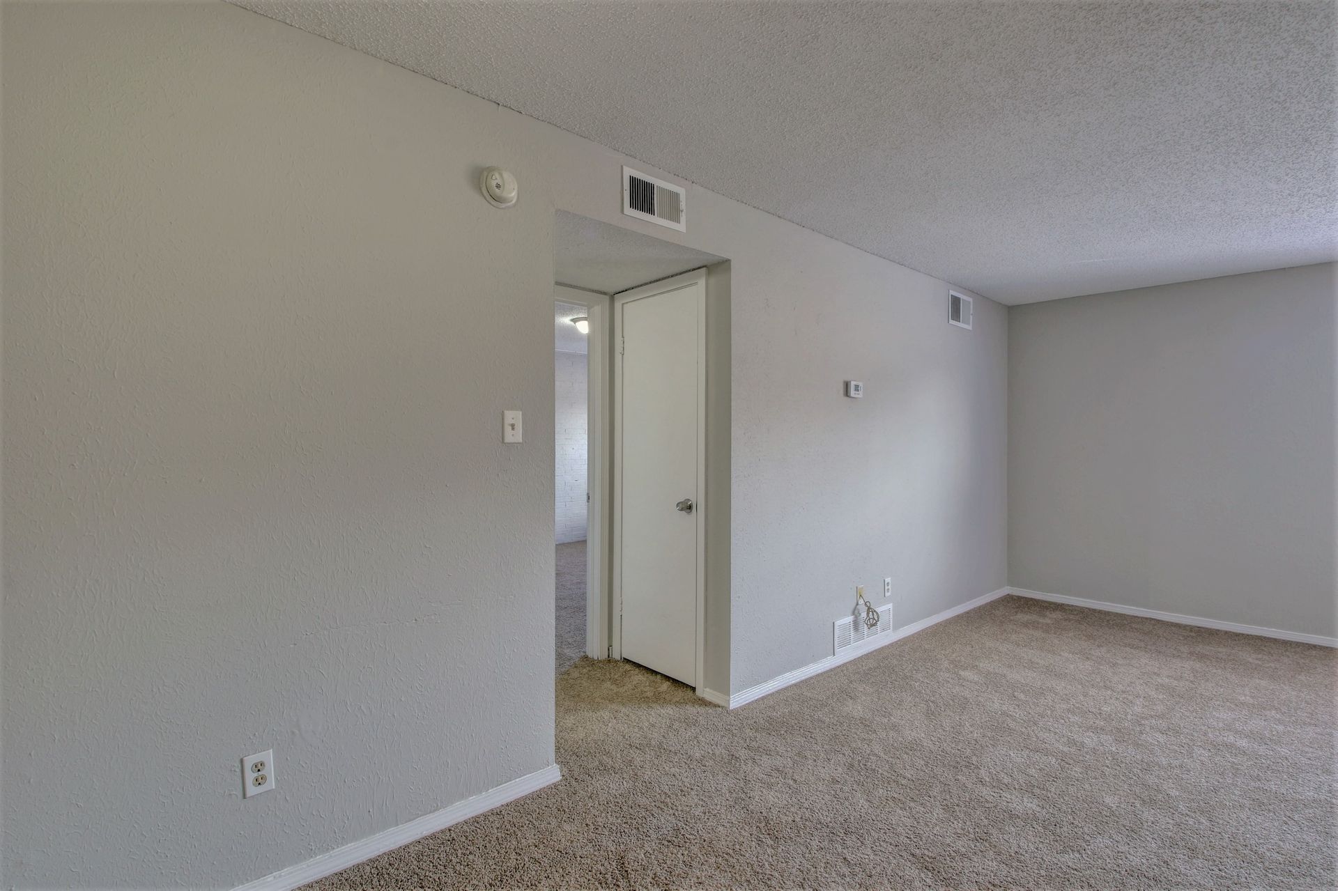 An empty living room with a carpeted floor and white walls.