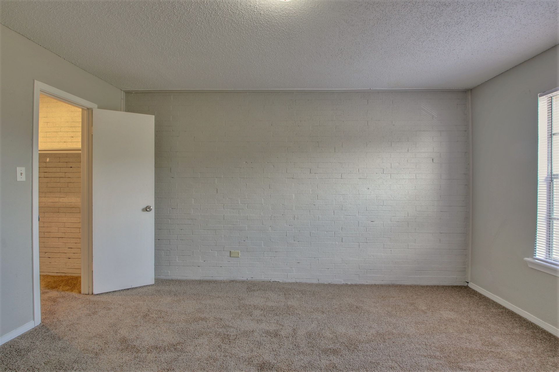 An empty bedroom with a brick wall and a window.