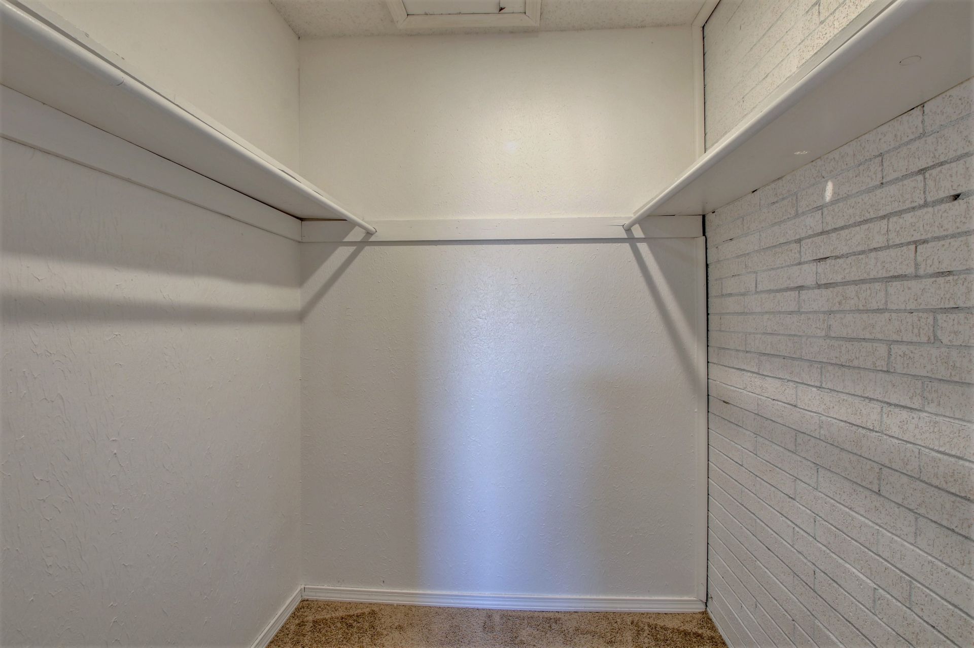 An empty walk in closet with white shelves and a white brick wall.