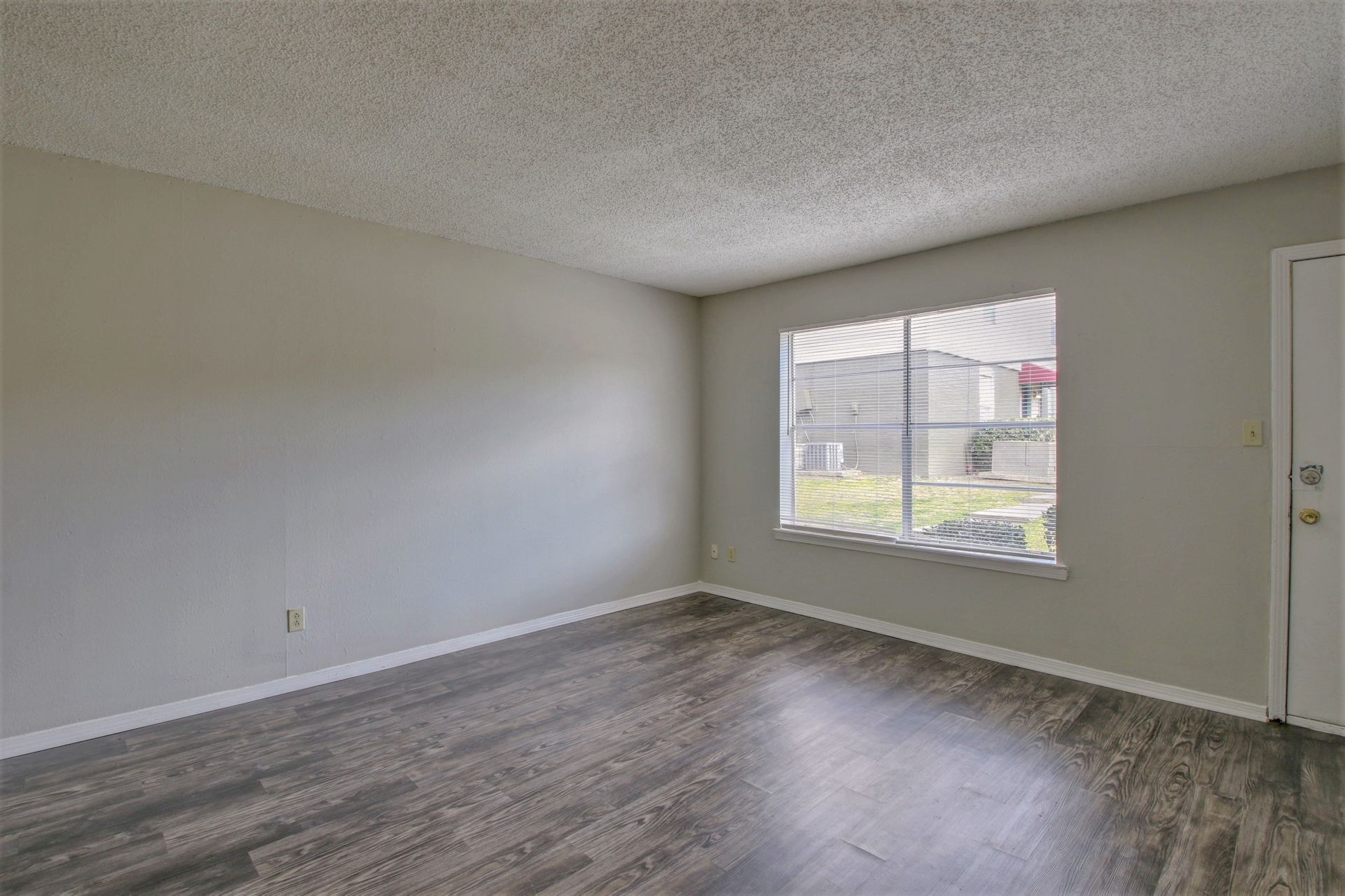 An empty living room with hardwood floors and a large window.