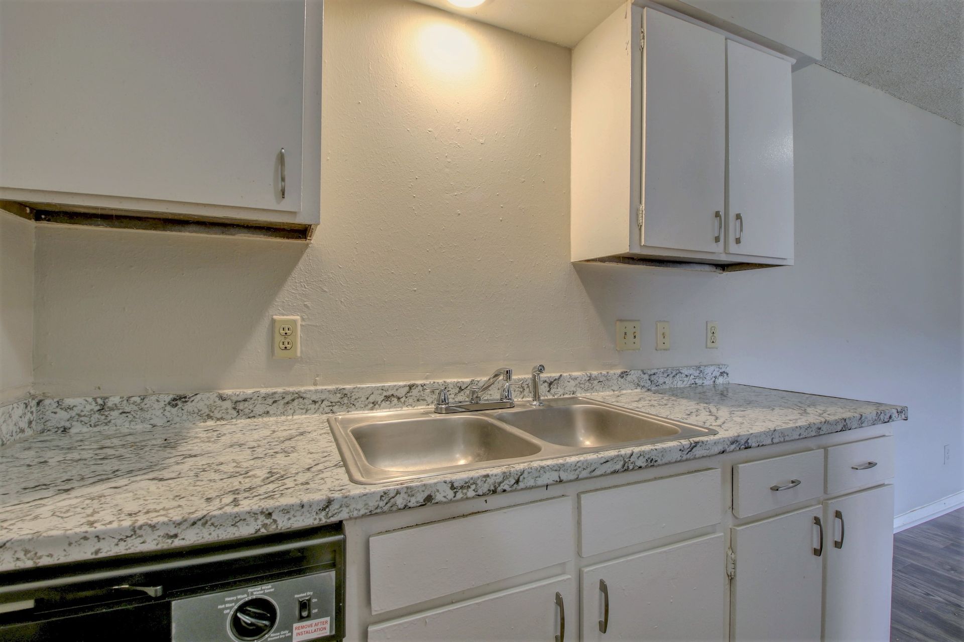 A kitchen with white cabinets , a stainless steel sink , and a dishwasher.