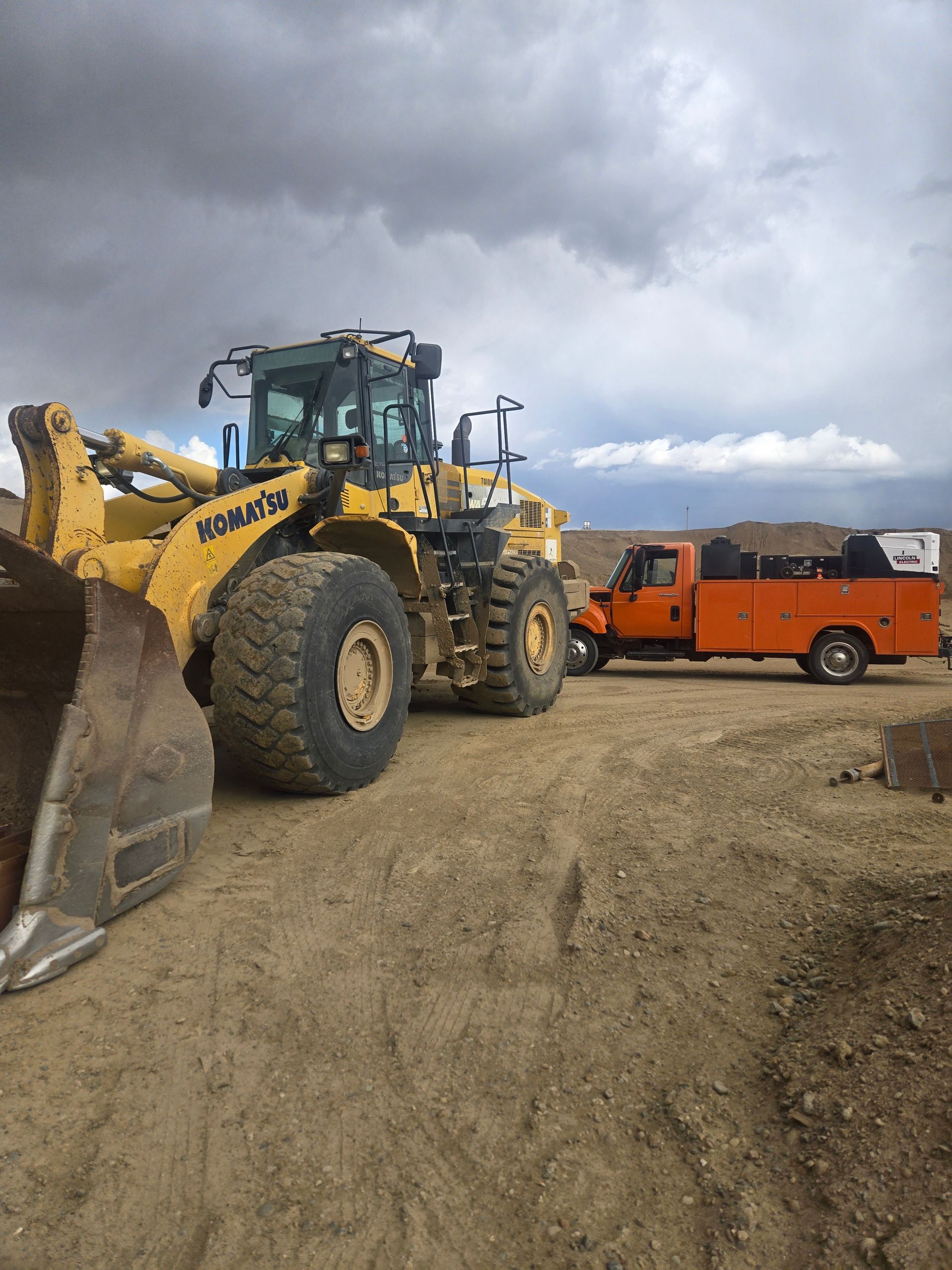A bulldozer is parked next to a truck in a dirt field.
