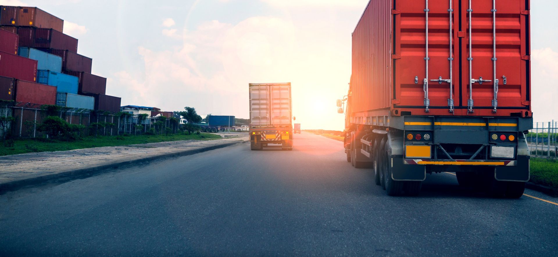 A row of semi trucks are driving down a highway at sunset.