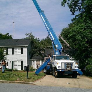 A blue truck with a crane attached to it is parked in front of a house.