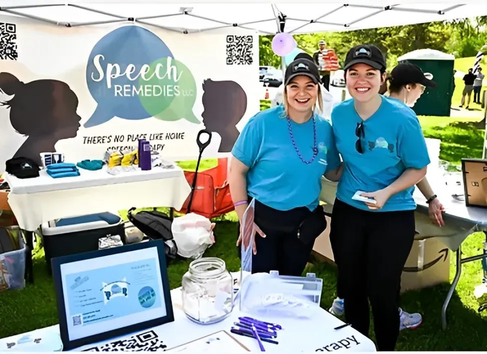 Two women standing in front of a speech remedies tent