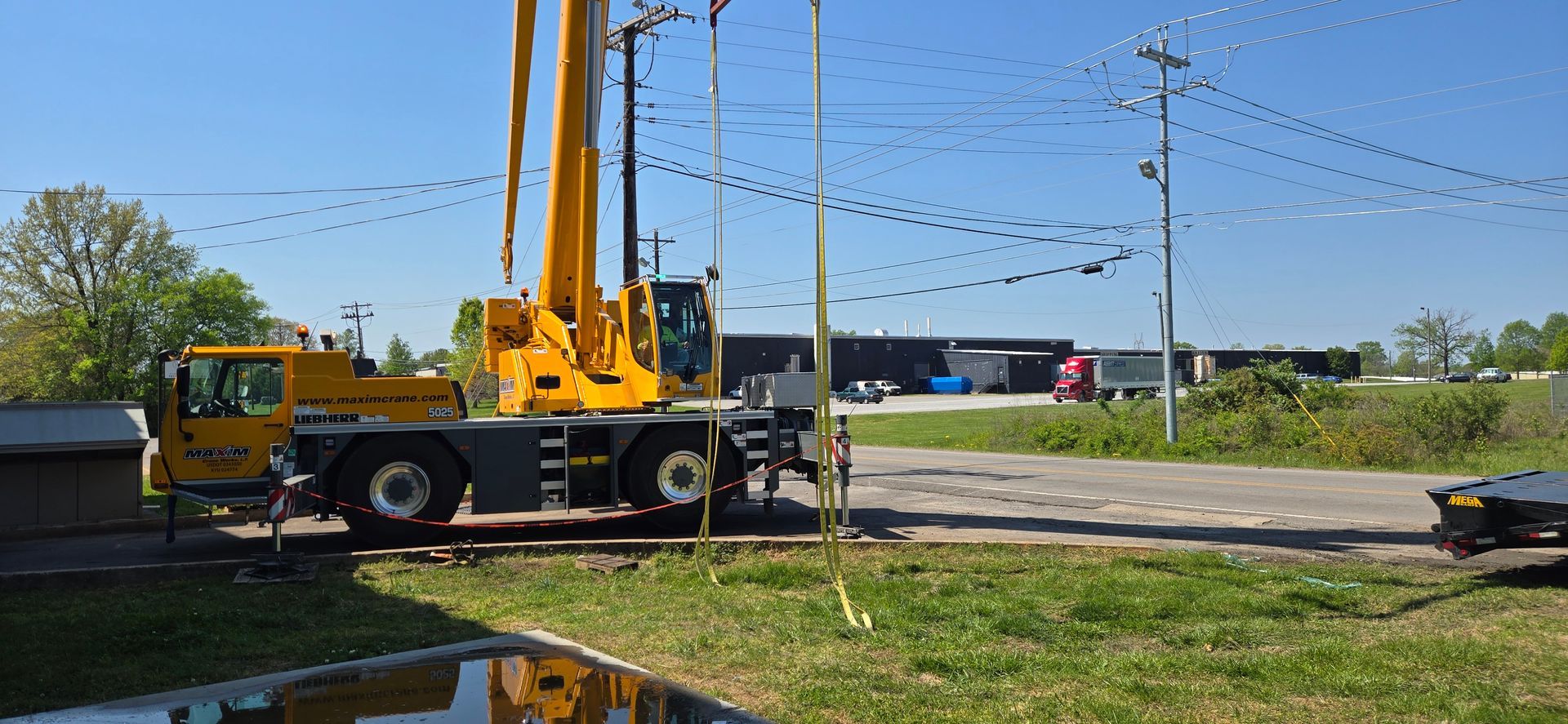 Yellow crane truck parked by a road in a sunny open field