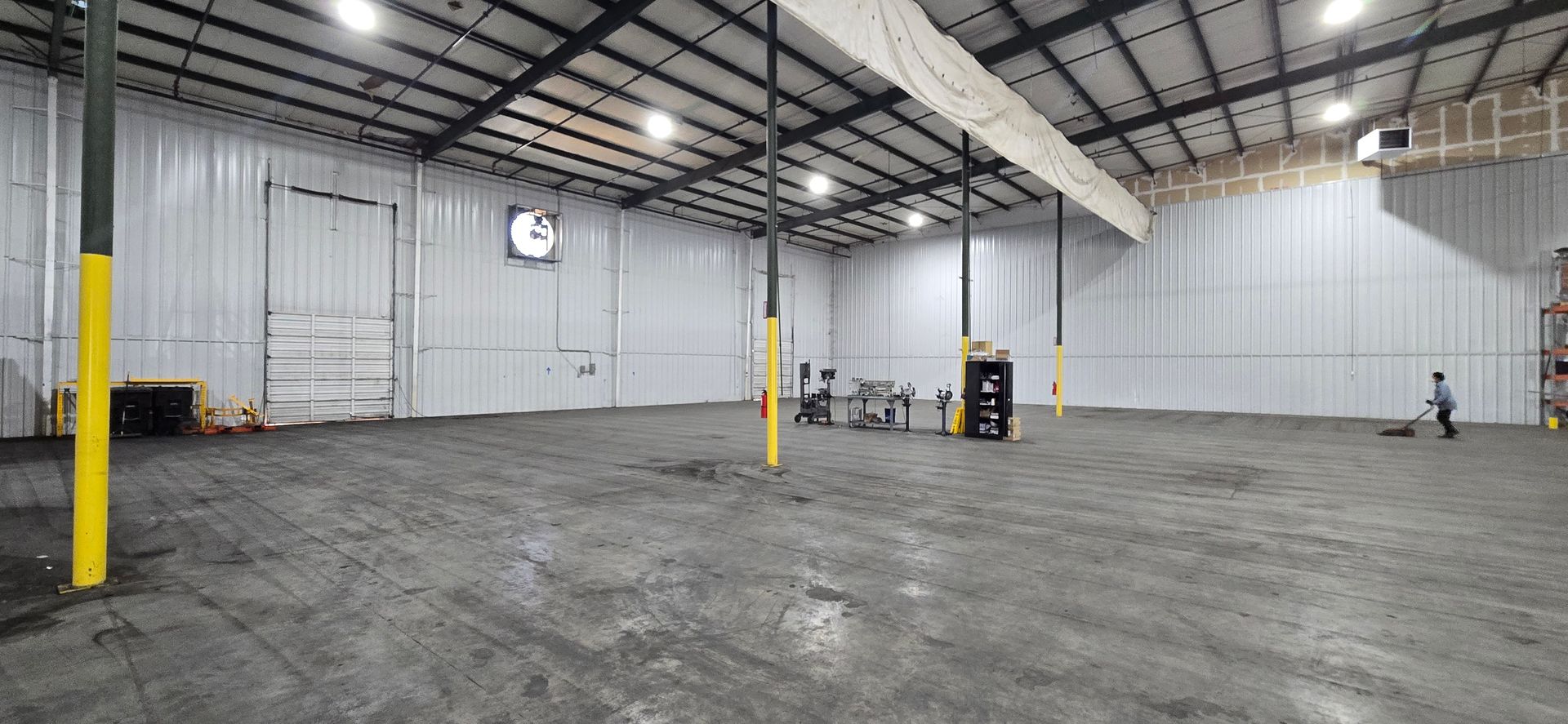 Large empty warehouse interior with concrete floor, metal walls, yellow pillars, and a few people near the far wall