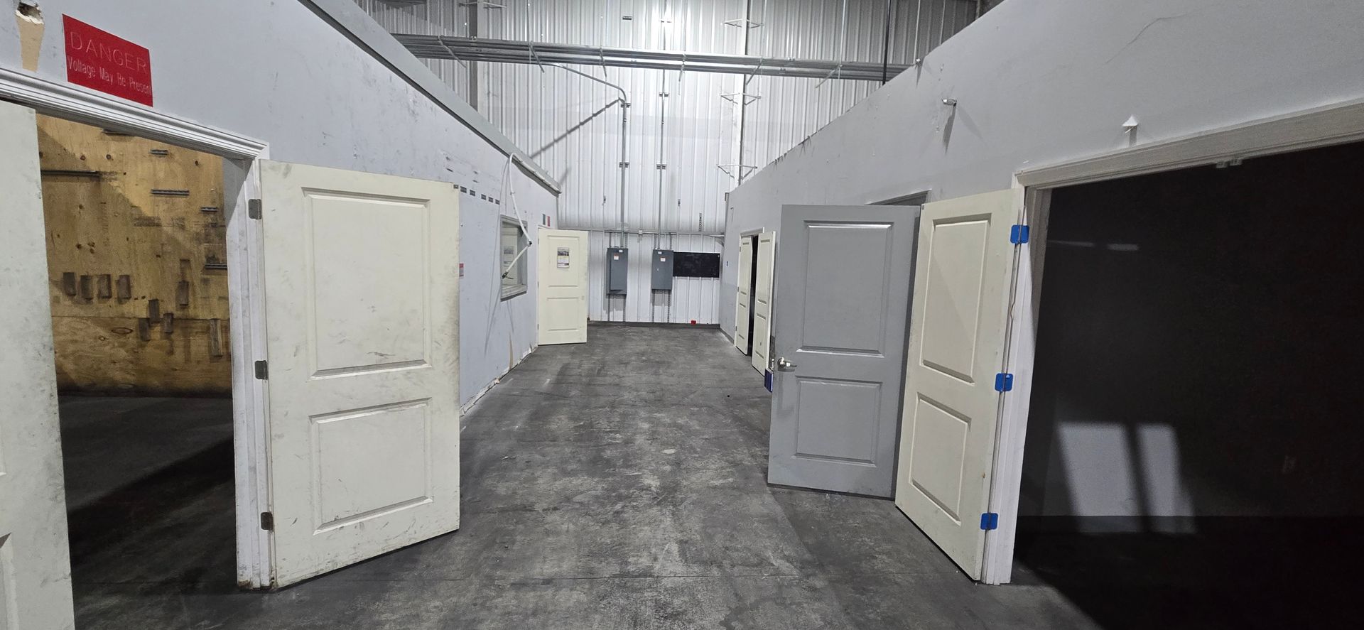 Wide warehouse aisle with several white doors standing open against metal walls.