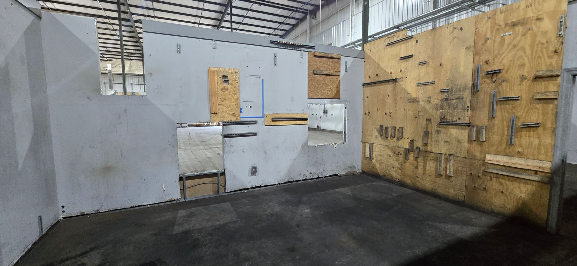 Indoor training room with plywood wall targets, gray barriers, and black padded floor