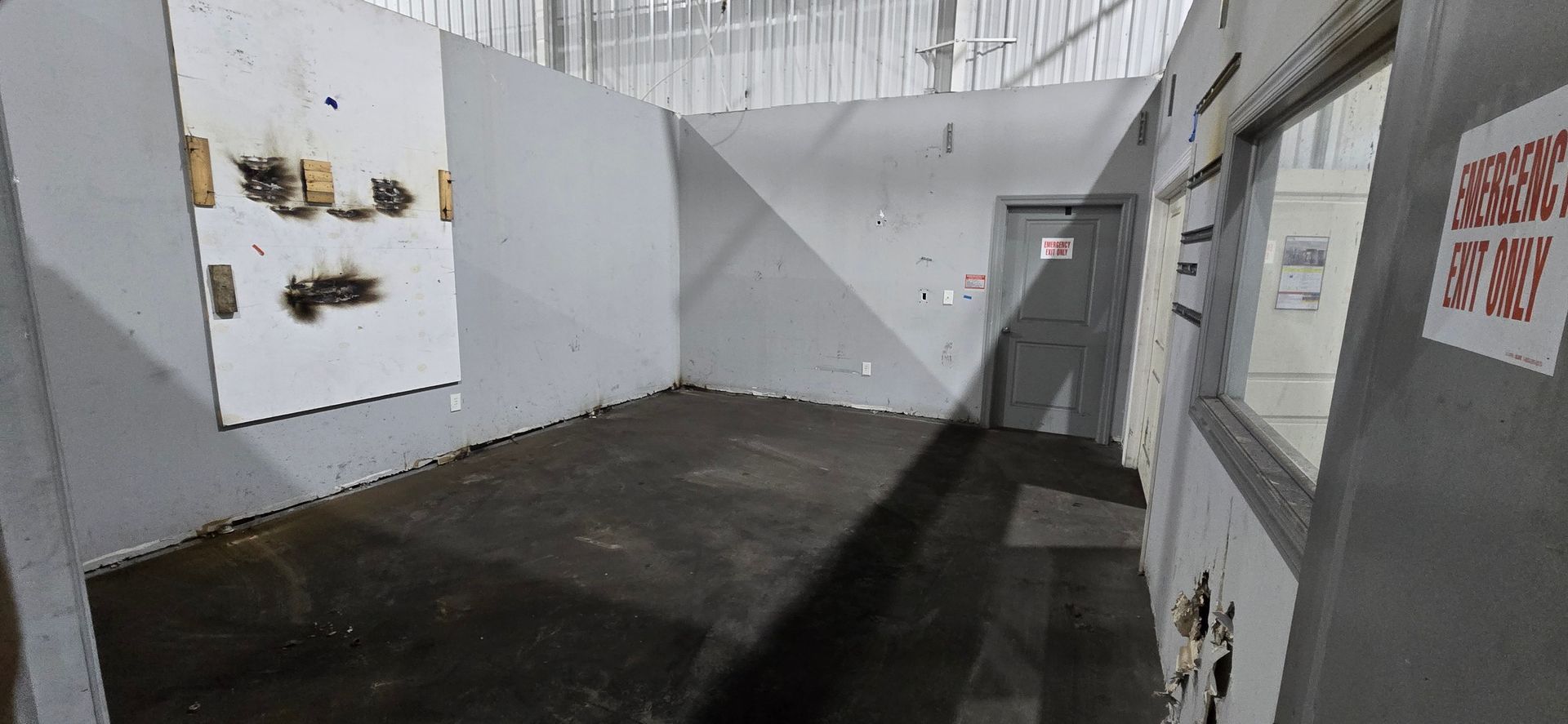 Narrow indoor hallway with white walls, dark floor, and windows on the right.