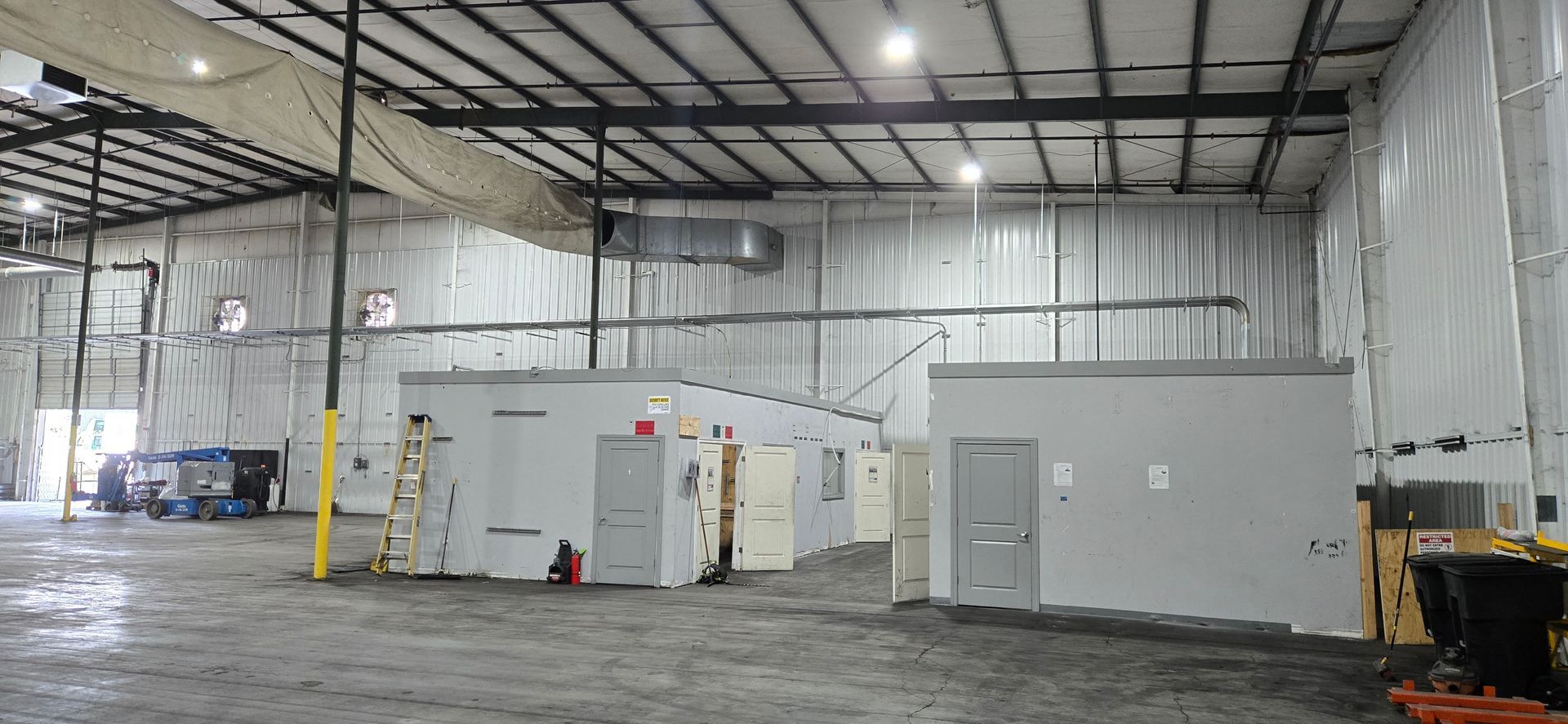 Spacious warehouse interior with gray modular offices and industrial equipment under a high metal ceiling.