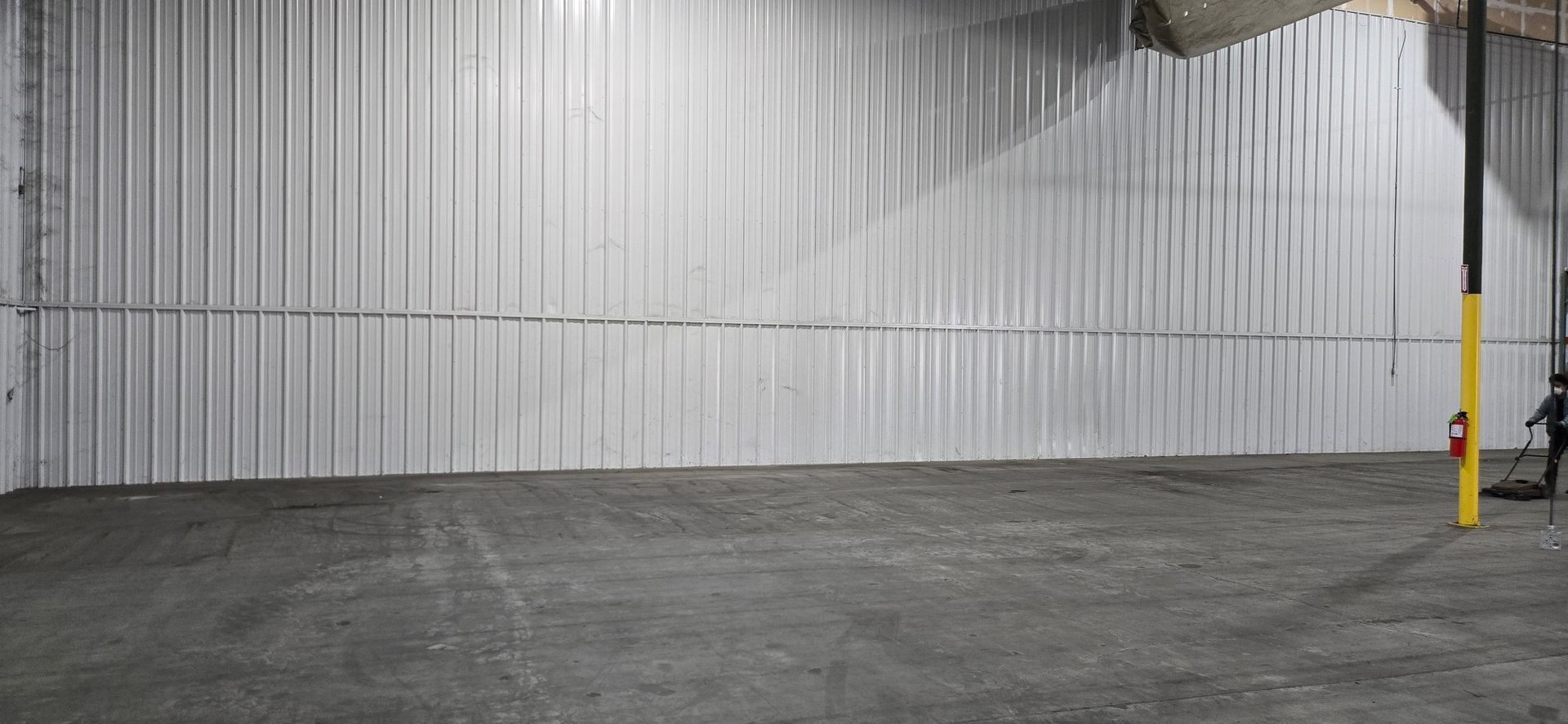 Empty warehouse with corrugated metal wall, concrete floor, and a yellow safety post