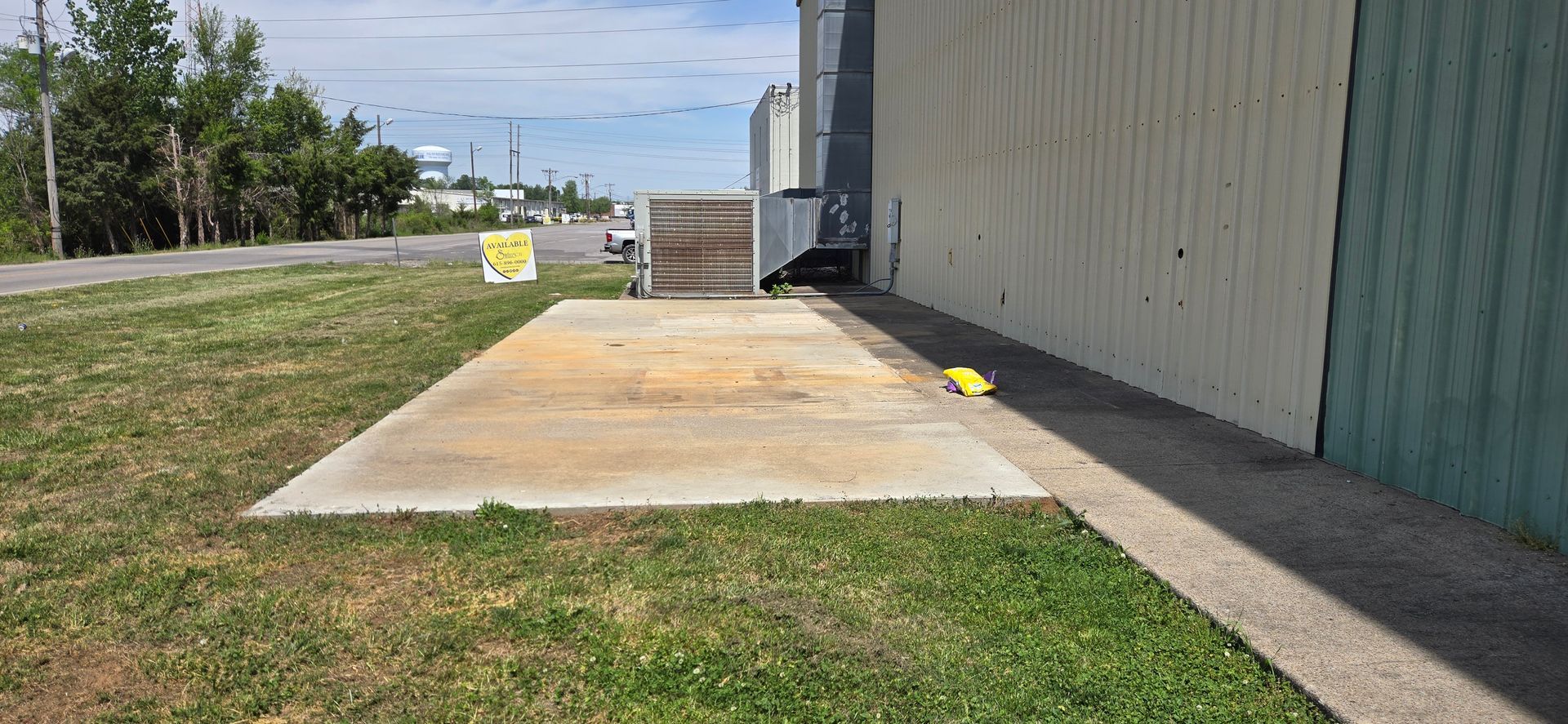 Concrete slab beside a metal building, with a grassy field and a small sign in the distance