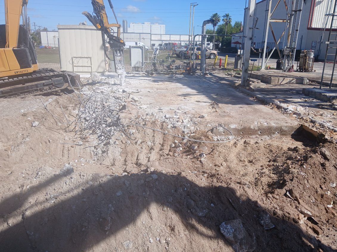 Construction site with excavator and rough dirt path beside industrial equipment and buildings