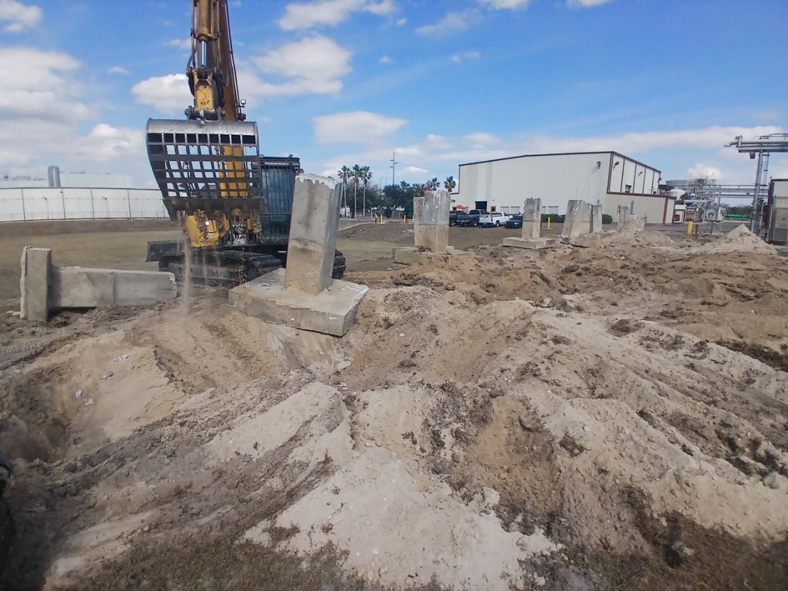 Construction site with excavator on muddy dirt and concrete blocks under a blue sky