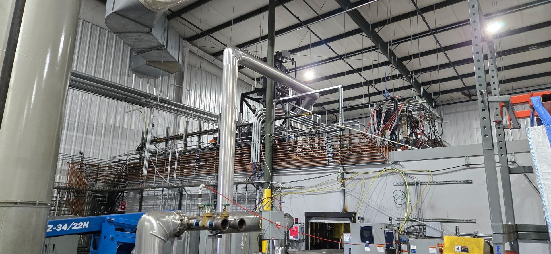 Industrial factory interior with metal piping, ducts, and machinery under a high ceiling