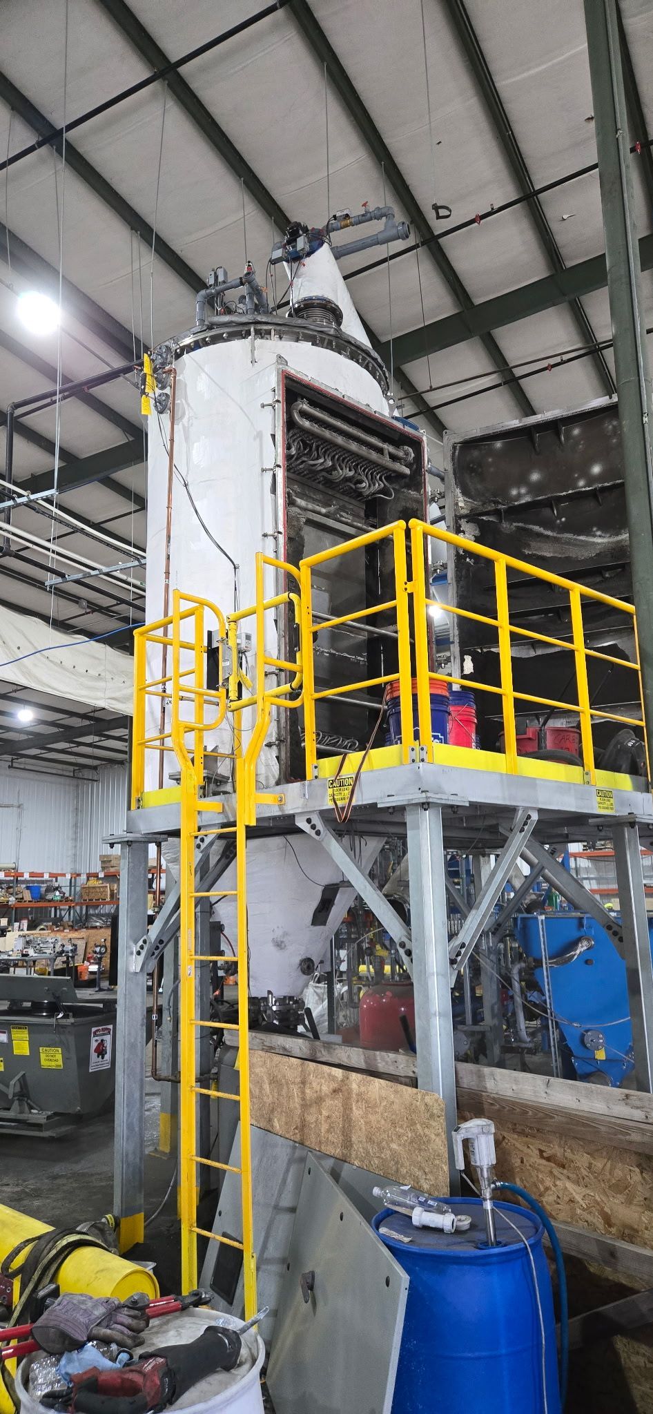 Industrial processing tank with yellow railings and ladder in a warehouse factory setting