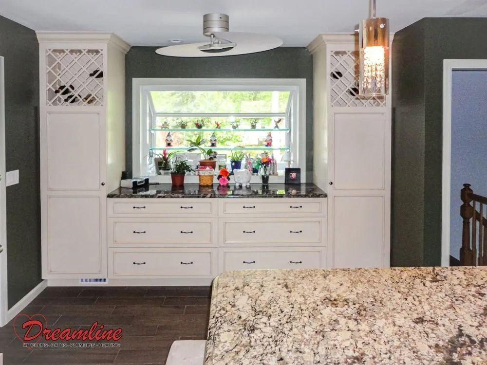 A kitchen with white cabinets , granite counter tops , a window and a ceiling fan.