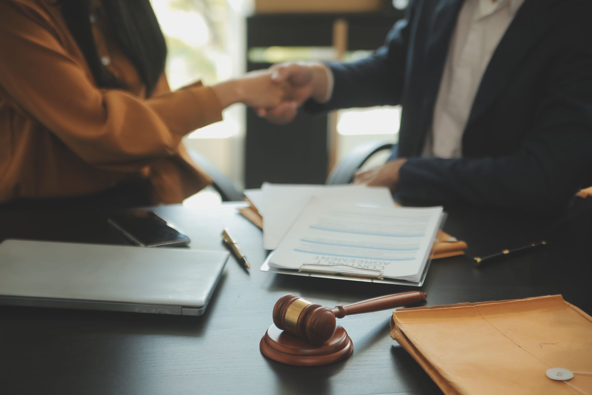 Two people shaking hands across a desk with documents and a gavel in a legal office
