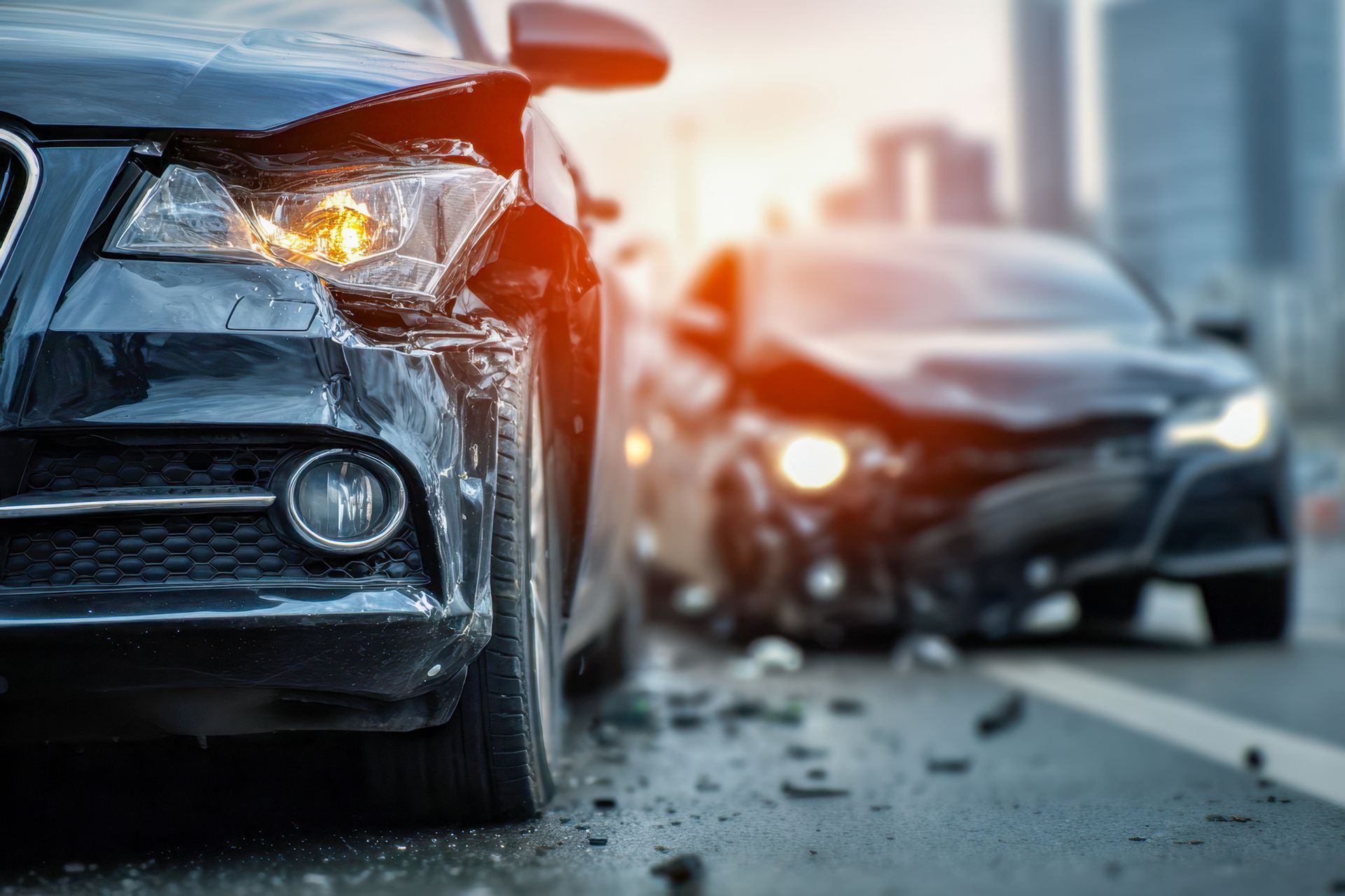 Two black cars involved in a head-on collision on a city street, headlights on, visible damage.