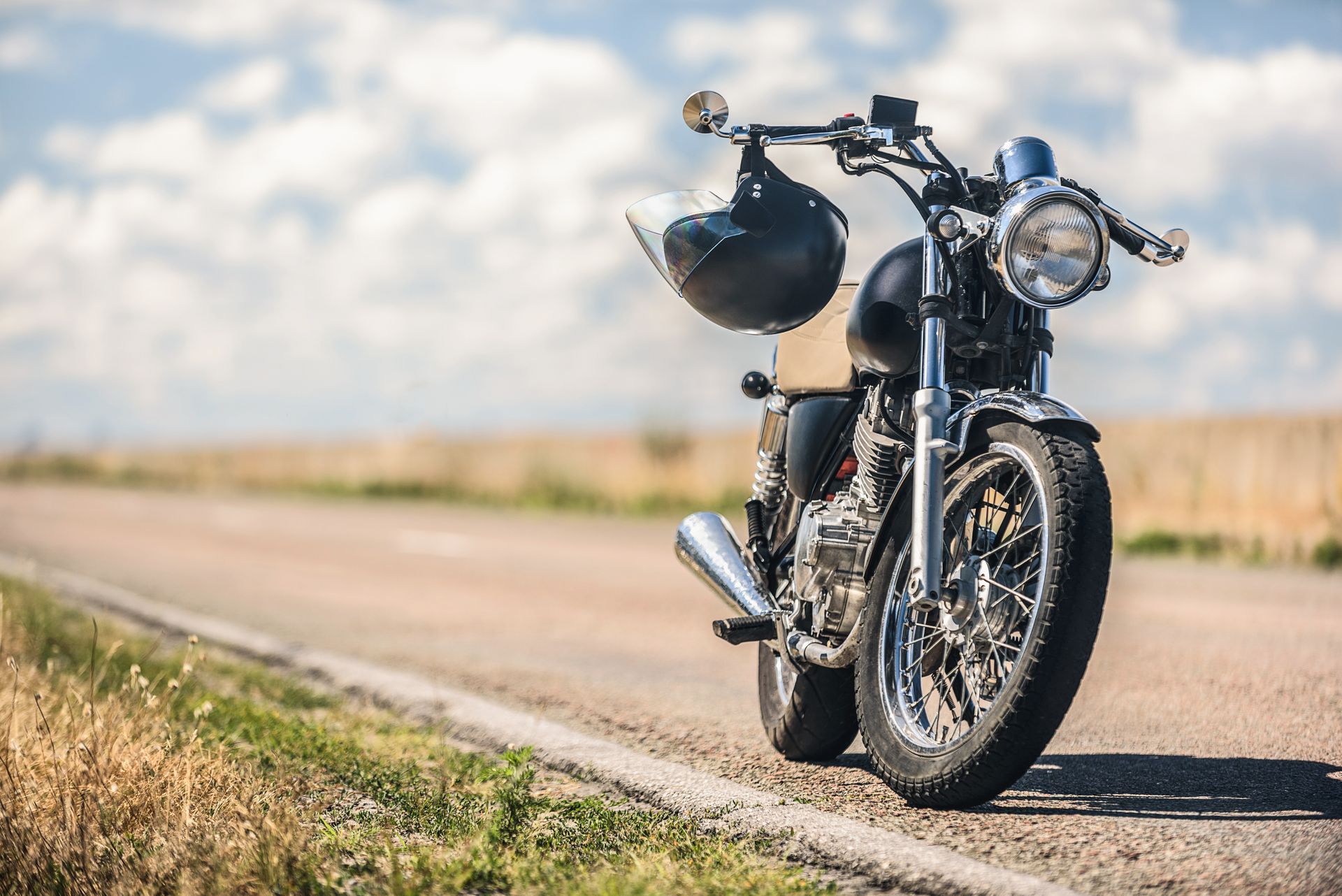 Black motorcycle with helmet, parked on a road beside a field, sunny day.