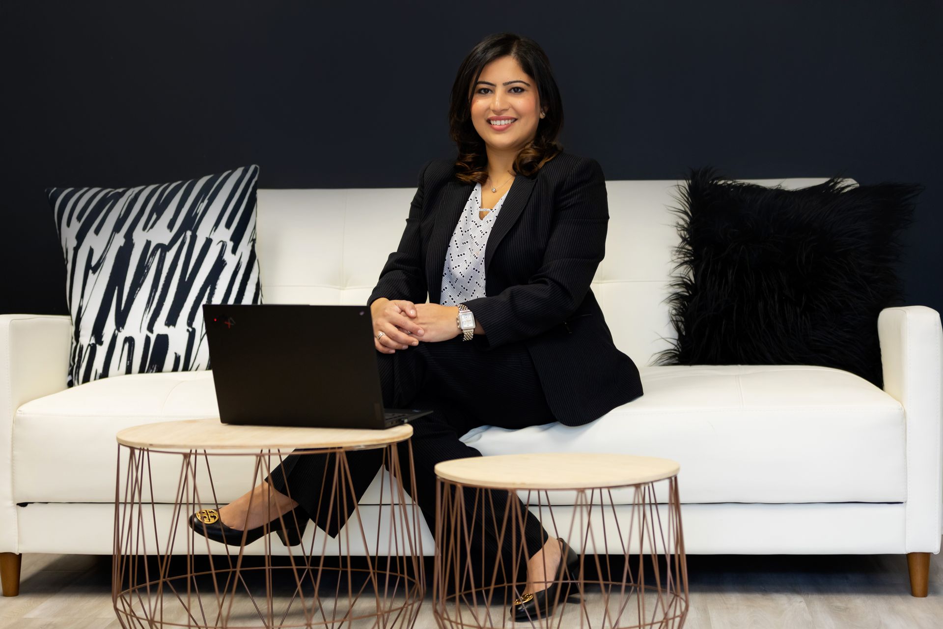 A woman is sitting on a sofa with a laptop on a table in front of her