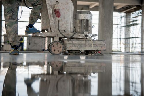A person using a floor polishing machine on a smooth, reflective concrete surface inside a construction site.