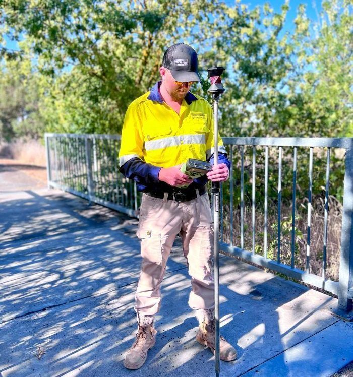 A Man In A Yellow Shirt Is Standing On A Bridge Holding A Pole — Point to Point Surveying In Yarrawonga, VIC
