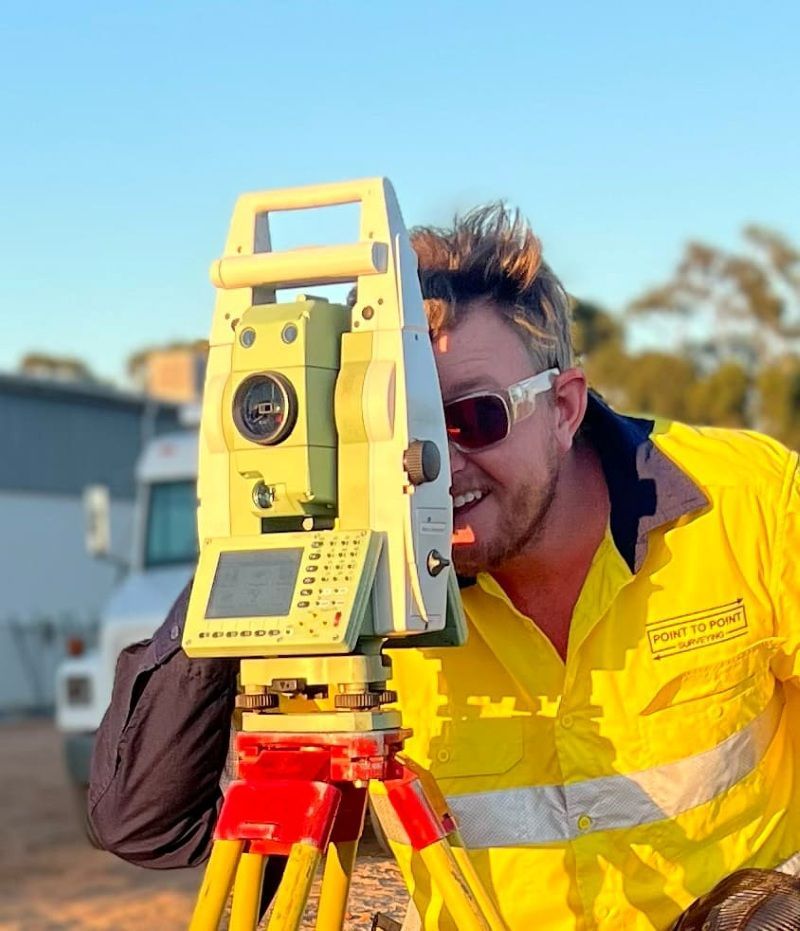 A Man In A Yellow Shirt Is Looking Through A Telescope — Point to Point Surveying In Tatura, VIC