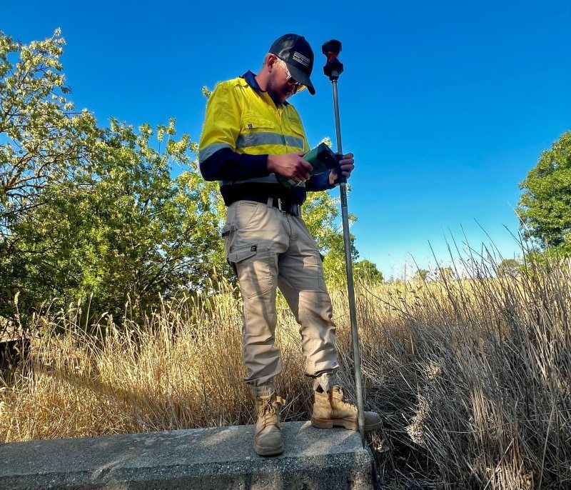 A Man In A Yellow Safety Vest Is Standing In A Field Holding A Pole — Point to Point Surveying In Yarrawonga, VIC