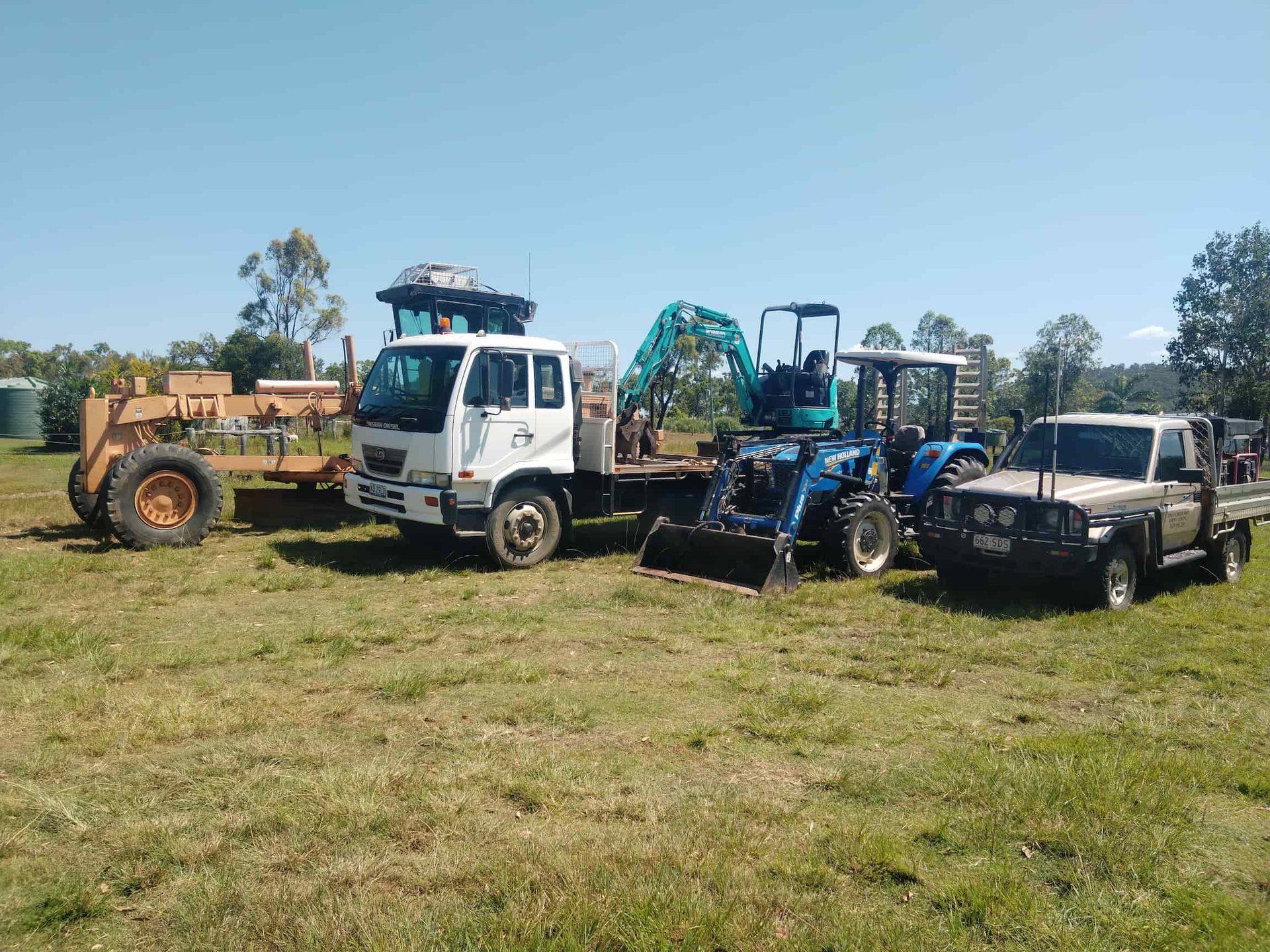 Cars and Excavator Lined Up On Grass — Mini Excavator Hire & Rural Fencing In Bungundarra, QLD