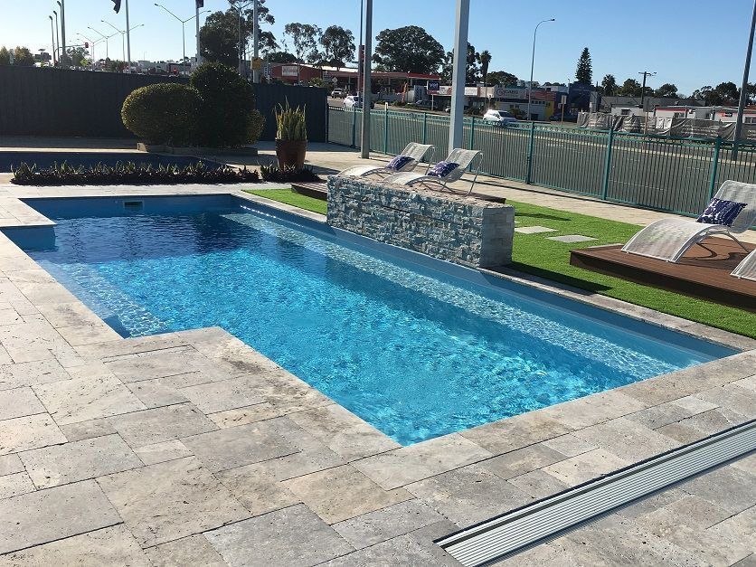 Backyard swimming pool with blue water, stone deck, lounge chairs, and a small waterfall feature