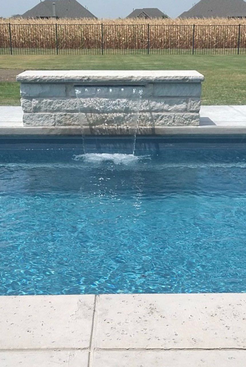 Backyard swimming pool with blue water, stone ledges, and black fire bowls along a wooden fence